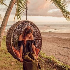 a woman sitting in a hanging chair on the beach with palm trees and ocean in the background