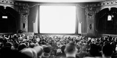 an auditorium full of people sitting and standing in front of a large window