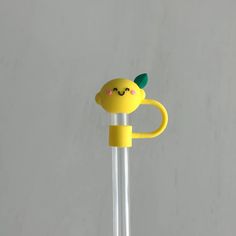 a yellow toy with a green leaf on it's head is standing in front of a gray wall