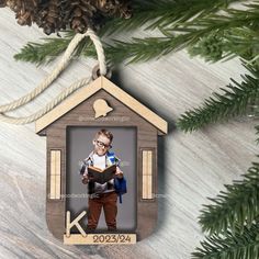 a christmas ornament with a boy reading a book in front of a pine tree