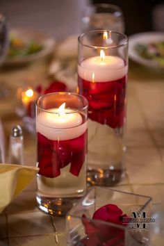 two candles sitting on top of a table filled with water and red roses in vases