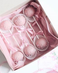 pink cake pops in a white box with ribbon on the top and bow around them