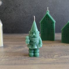 a candle with a green gnome figure next to some small houses on a wooden table