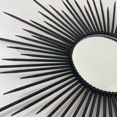 a circular mirror made out of black needles on a white surface with a reflection in the center