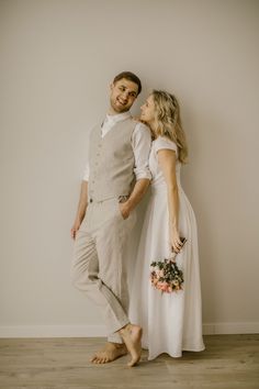 a man and woman standing next to each other in front of a white wall holding flowers