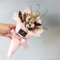 a person holding a bouquet of flowers in a pink paper cone with ribbon around it