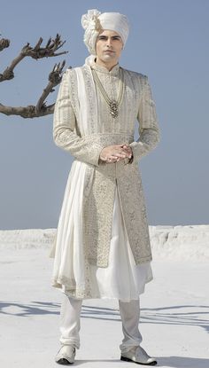 a man dressed in white standing next to a tree and wearing a turban