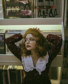 a woman wearing glasses standing in front of a book shelf