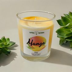 a candle that is sitting on a table next to some plants and leaves, with the words mango written in spanish