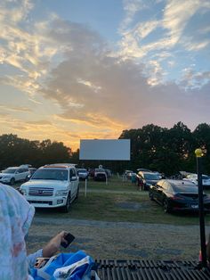 a person sitting on a bench in front of a movie screen with cars parked behind it