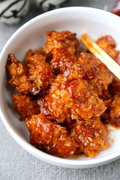 a white bowl filled with meat and chopsticks on top of a gray table