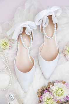 a pair of white shoes with pearls and flowers on the floor next to a purse