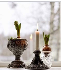 two vases with plants in them sitting on a window sill next to a candle