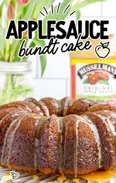 a bundt cake with icing sitting on top of a table next to a jar of applesauce