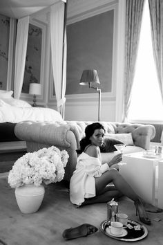 a woman sitting on the floor in front of a couch with flowers and other items around her