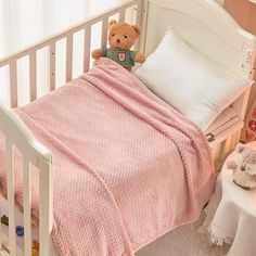 a teddy bear sitting on top of a pink blanket in a white crib next to pillows