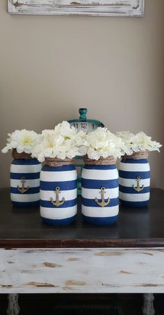 four blue and white striped jars with flowers in them on a table next to a clock