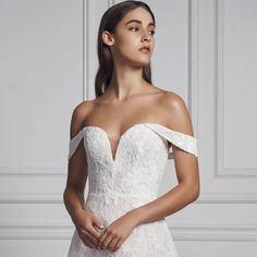 a woman in a white wedding dress with an off the shoulder neckline and sleeves