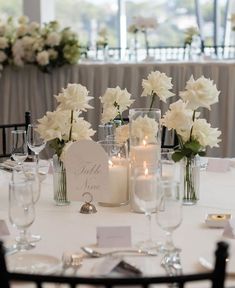 the table is set with white flowers, candles and place cards for guests to sit at