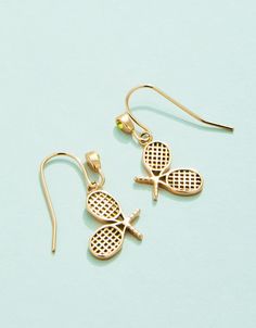 two tennis racquets dangling from earrings on a light blue background with gold ear wires