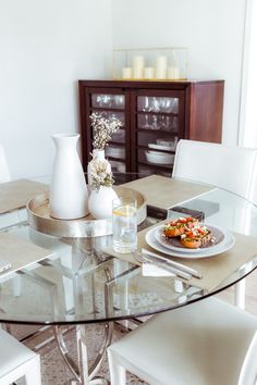 a glass table with white chairs around it and a vase filled with flowers on top