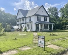 a large white house sitting in the middle of a lush green field with a for sale sign next to it