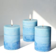 three blue candles sitting next to each other on a white surface with the light shining through them