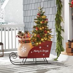 a christmas tree in a sleigh with presents on the front porch next to it