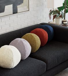 a black couch with four different colored pillows on it's back and one has a white brick wall in the background