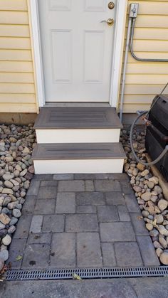 two steps leading up to a white door on a yellow house with gravel and rocks