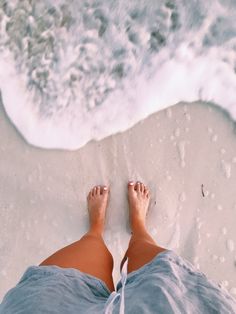 a person standing on the beach with their feet in the sand and water behind them