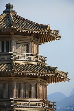 a tall wooden building with a clock on the top of it's tower and mountains in the background