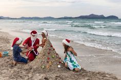 three children are playing in the sand at the beach while santa is building a christmas tree