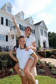 two women are posing in front of a large house