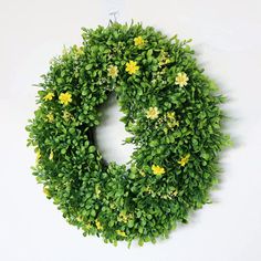 a green wreath with yellow flowers hanging on a wall