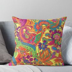 an orange and pink pillow with colorful paisley print on the front, sitting on a couch