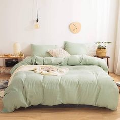 a bed with green sheets and pillows in a white room next to a wooden floor