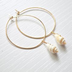 a pair of gold hoop earrings with shells hanging from the ends on a white surface