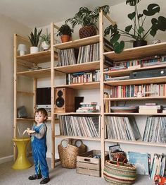 a kid standing in front of a bookshelf filled with records