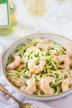 a bowl filled with zucchini noodles and shrimp next to a bottle of wine