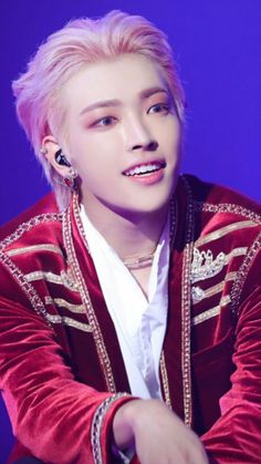 a man with pink hair and piercings wearing a red velvet jacket is looking at the camera