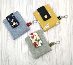 three small wallets sitting on top of a wooden table next to each other with keychains