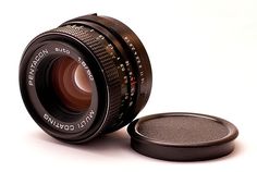 an old camera lens sitting on top of a white surface next to a small round object