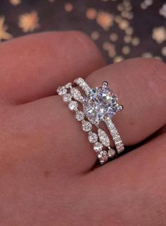 a woman's hand with a diamond ring on top of her finger and the other hand holding an engagement ring