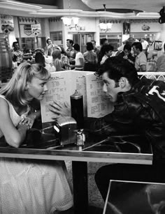 a man and woman sitting at a table in a restaurant looking at each other's menus