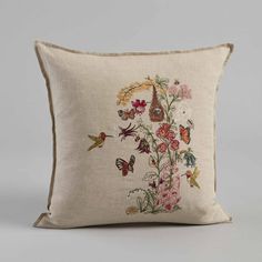 a decorative pillow with embroidered flowers and birds on the front, sitting on a grey background