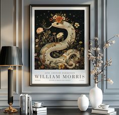 a framed poster with a snake and flowers on the wall above a table next to a lamp