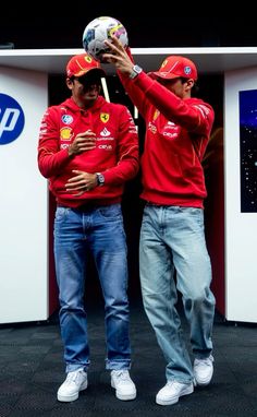 two men standing next to each other in front of a wall with a soccer ball on it