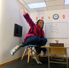 a woman sitting on top of a chair in front of a whiteboard with writing on it