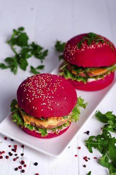 two red burgers with lettuce and tomato on a white plate next to parsley